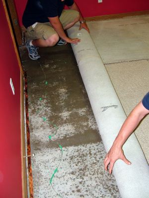 Atkinson water damaged carpet being removed by two men.